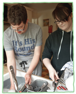 Adult care client washing-up with with care staff member drying.