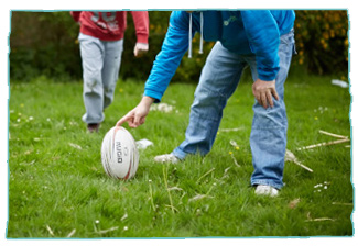 Care staff member holding a rugby ball for young care client to kick